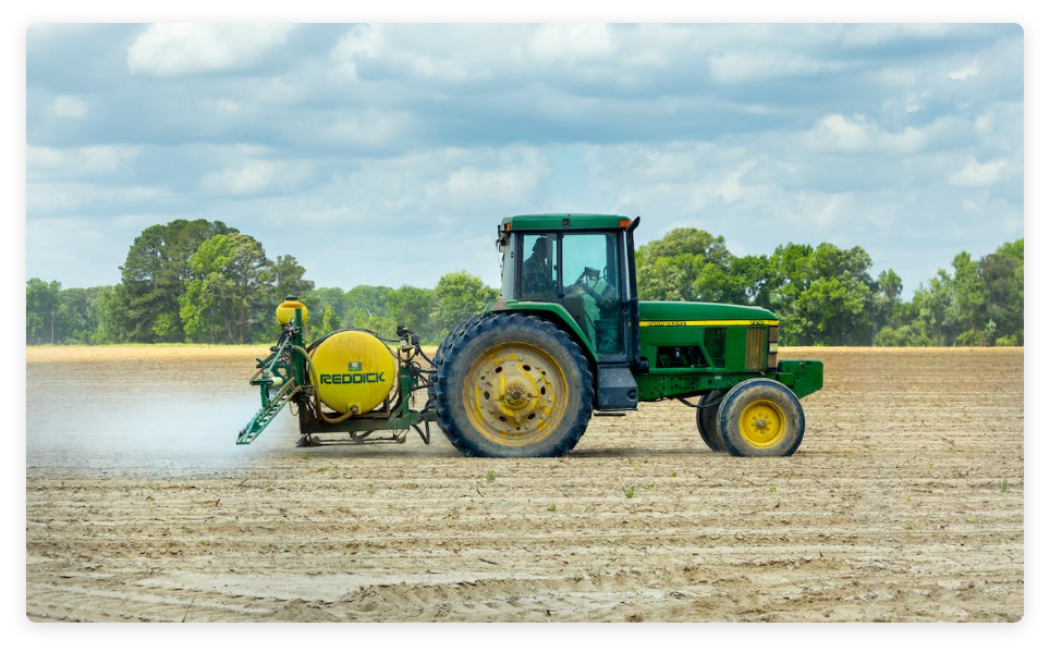 Green tractor driving over a recently plowed dirt field while spraying pesticides from back end tractor attachment.