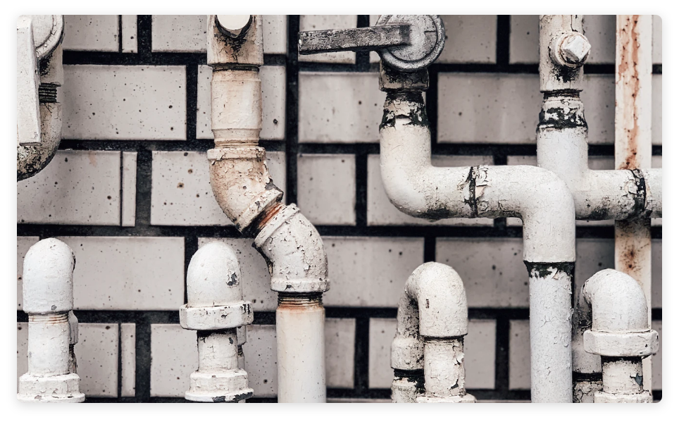 Detail of water pipes and valves crossing paths over a white brick background.